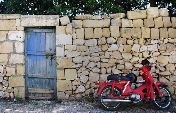 Rotes Moped, angelehnt an helle Bruchsteinmauer mit blauer Holztür