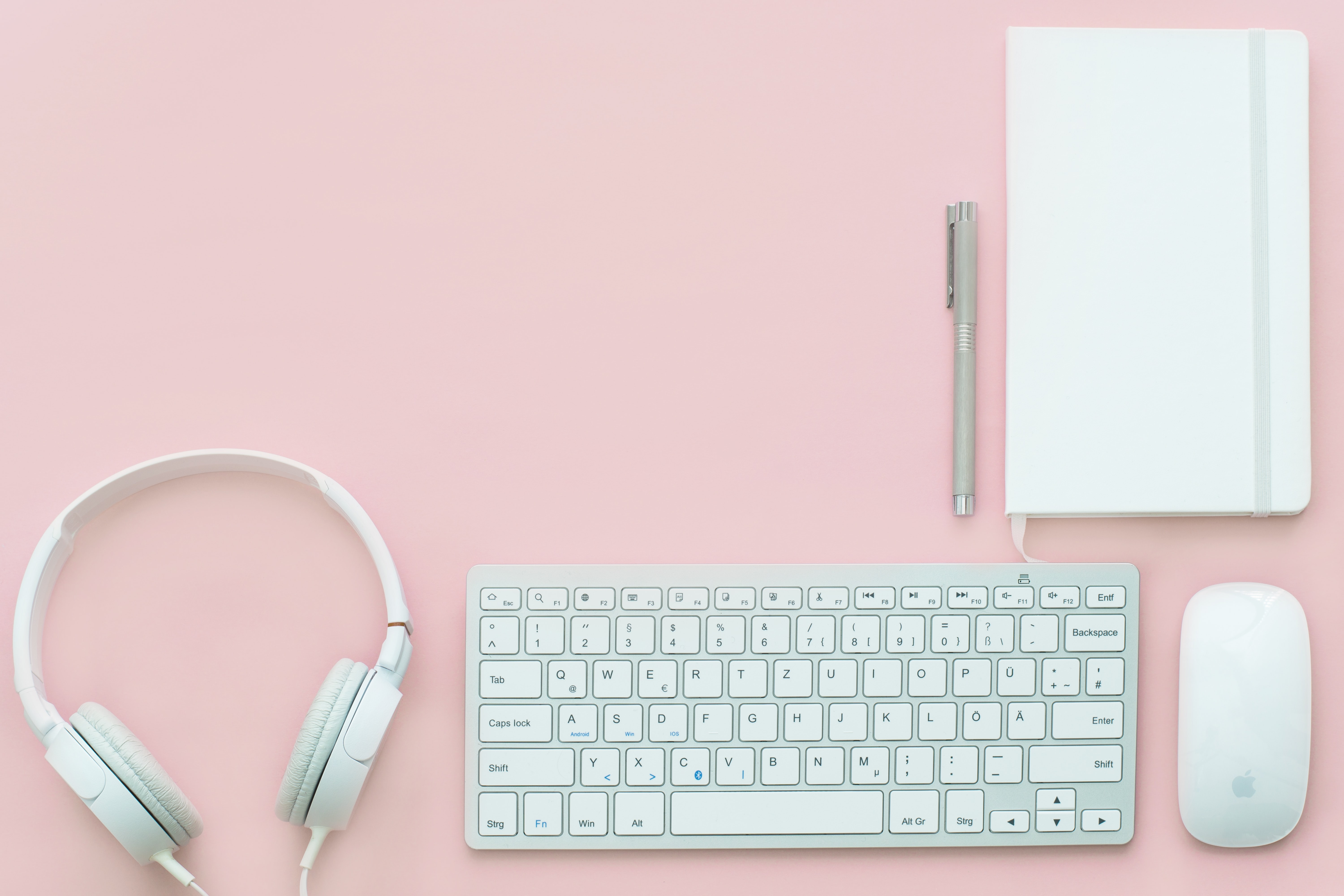 Headset, Tastatur, Maus und Notizblock in weiß vor rosa Hintergrund